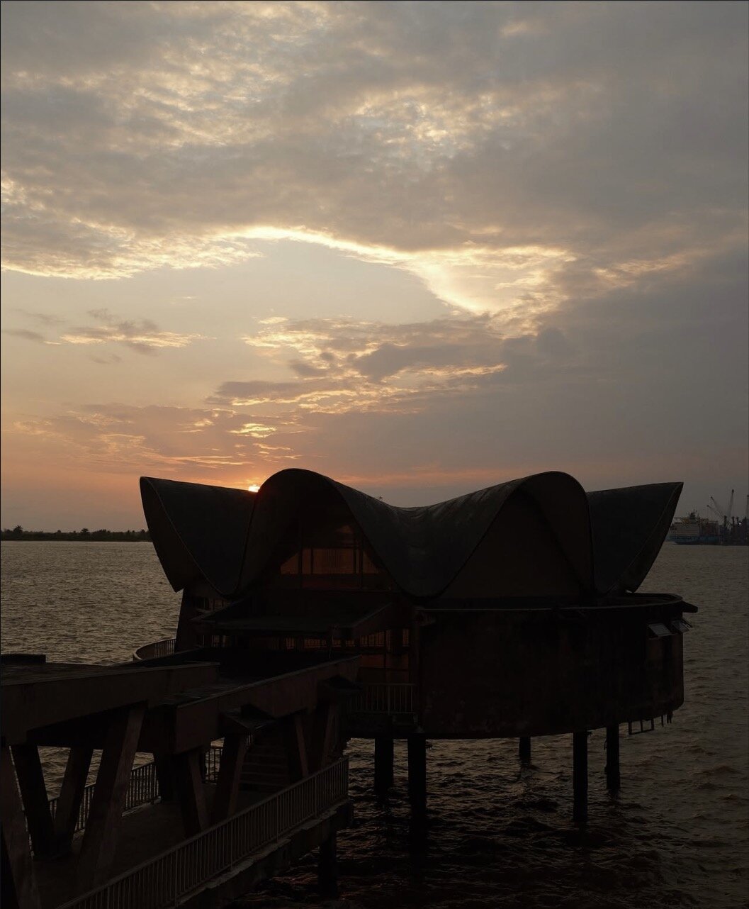 Sunset over the water at the Nahous building, Lagos, with its distinctive curved roof silhouetted against the sky